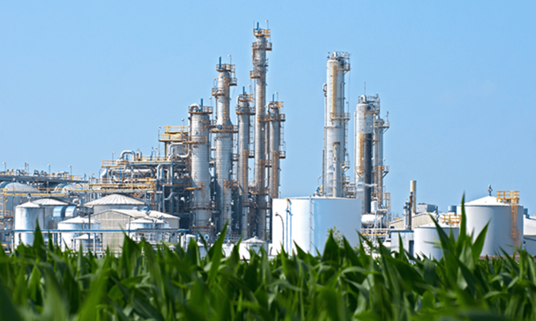 a factory with tall towers and a corn field