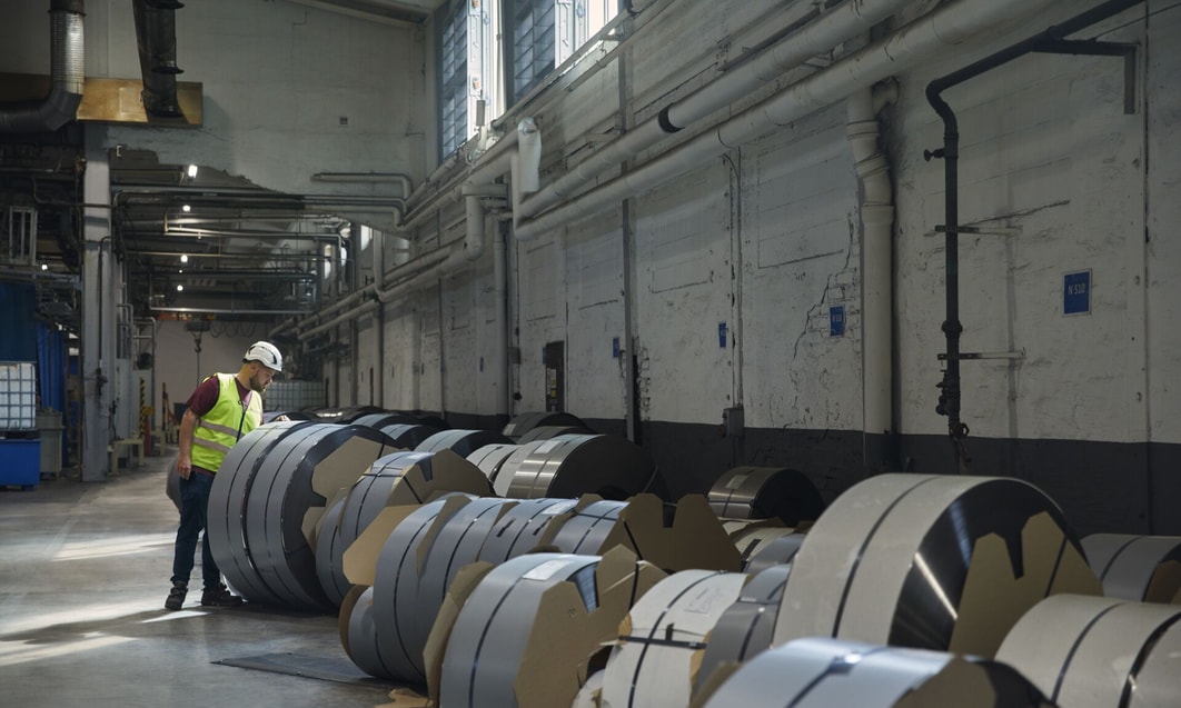 a person in a factory with rolls of steel