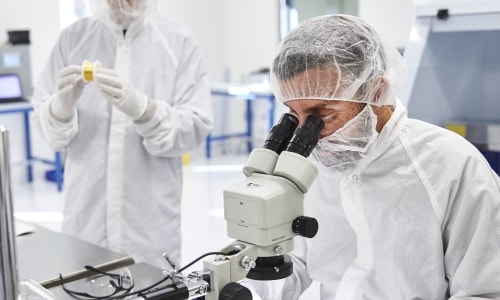 a few people in white coats looking through a microscope